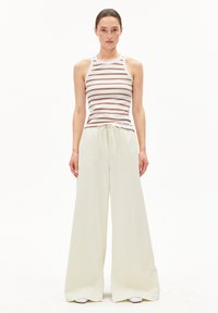 Streepjesshirt in wit en bruin gecombineerd met wijde, off-white broek; zachte stof, relaxte fit, taillekoord en subtiele textuur.