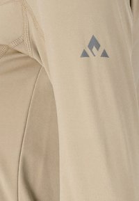 Light beige long-sleeve shirt with smooth texture. Features a gray geometric logo on the left sleeve, reinforced stitching along seams.
