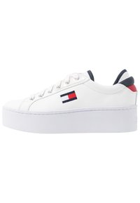 Sneaker en cuir blanc avec une semelle plateforme, dotée d'œillets argentés, d'un bout arrondi et d'une touche de couleur marine et rouge au niveau du talon.