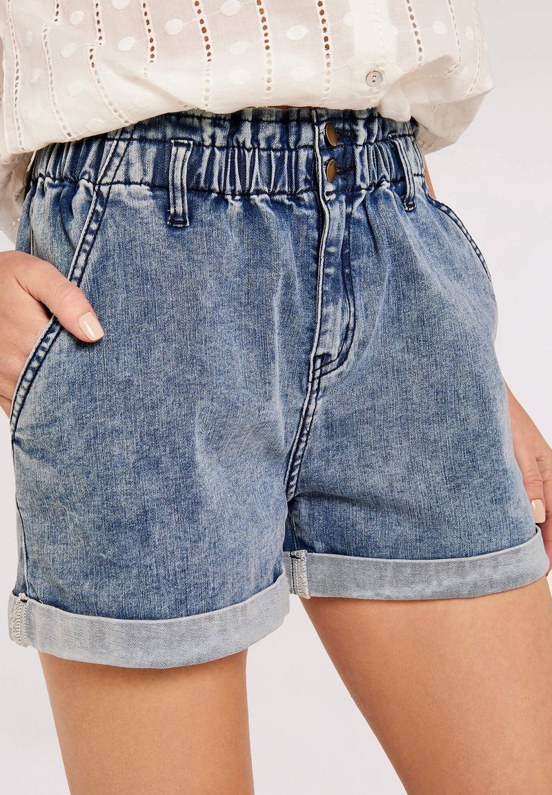 Jeans-Shorts mit einer hellblauen Waschung, ausgestattet mit einem elastischen Bund, umgeschlagenen Säumen, zwei Seitentaschen und zwei vorderen Knopfverschlüssen.