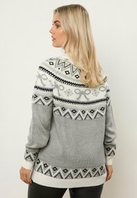 Pull en tricot gris avec des motifs géométriques blancs et noirs, col rond, manches longues, et poignets et ourlet côtelés. Texture douce, design décontracté.