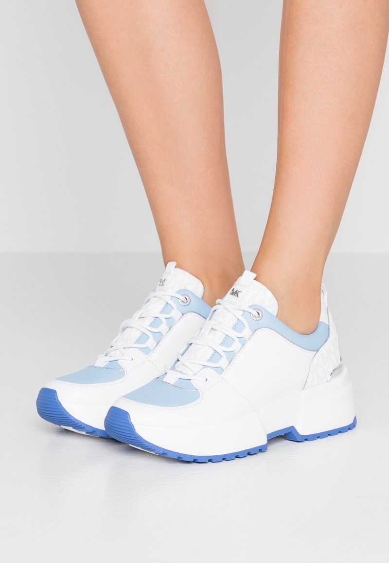 Vita och ljusblå sneakers med en texturerad bakpanel, kraftig sula och kontrasterande blå gummidetaljer. Snörningsdesign med metalöglor.