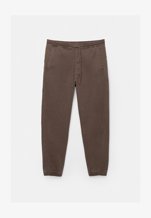 Brązowe spodnie dresowe z miękkiego materiału, z elastycznym pasem ze sznurkiem, dwoma bocznymi kieszeniami i zwężanymi nogawkami.