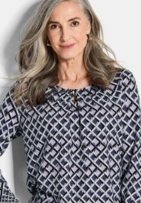 Langärmlige Bluse in Dunkelblau, mit einem geometrischen Muster aus lavendel- und hellblauen Quadraten, einem gerafften Ausschnitt und einer Schlüssel-Detailöffnung.