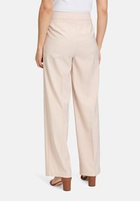 Pantalons larges beige avec une texture lisse, dotés d'une taille haute et de deux poches latérales. Remarquables par leur coupe ajustée et leurs plis.