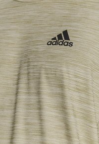 Beżowa tkanina z melanżem z czarnym logo Adidas nadrukowanym na górnej części koszulki.