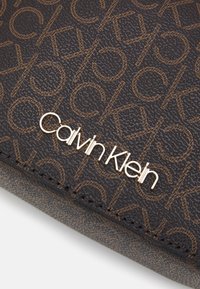 Borsa marrone testurizzata Calvin Klein con motivo a logo in rilievo e un accento in metallo dorato con logo sul davanti.