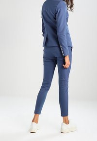 Modrý saka vestičkový oblek se přiléhavým blazerem se zadním rozparkem a slim-fit kalhotami, doplněný bílými teniskami. Hladký materiál a moderní design.