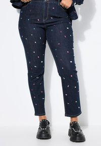 Tmavě modré džíny z denimu s barevnými flitry, slim fit a rovný střih. Doplněno černými masivními botami.