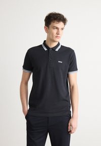 Crna polo majica s tri gumba, kontrastni svijetloplavi i bijeli prugasti ovratnik i manšete, te mali logotip na prsima.