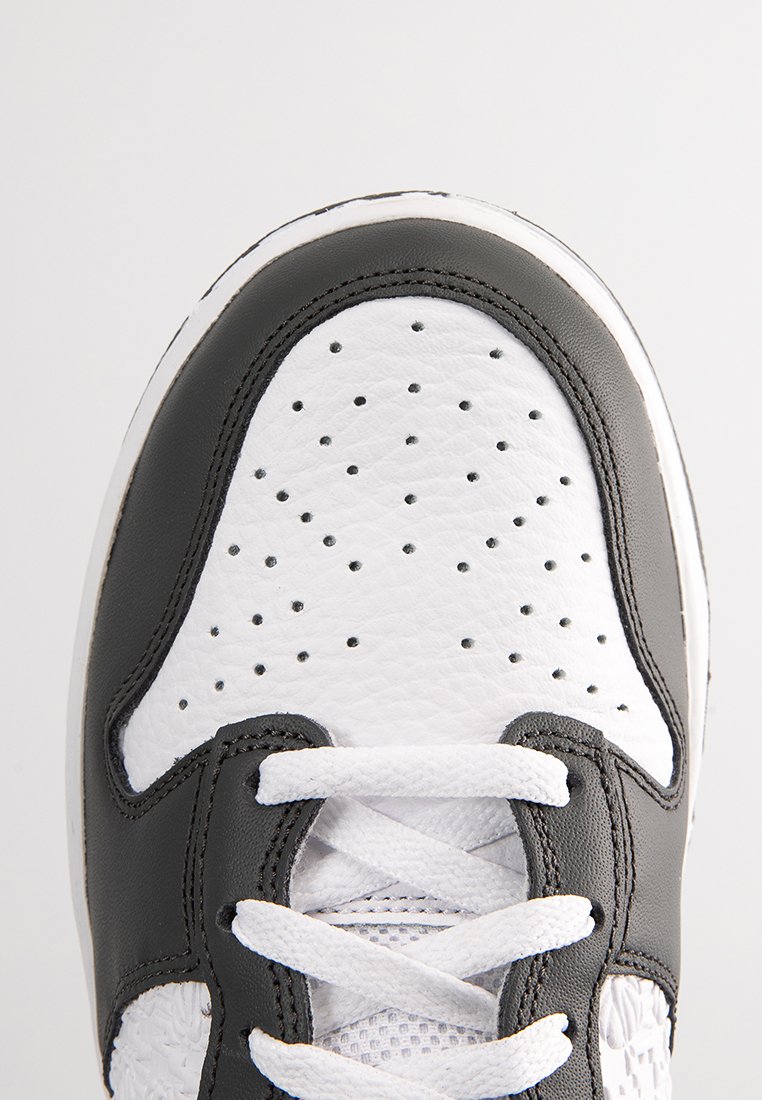 Gros plan sur l'avant d'une basket en cuir noir et blanc avec des perforations et des lacets blancs noués dans un motif en croix.