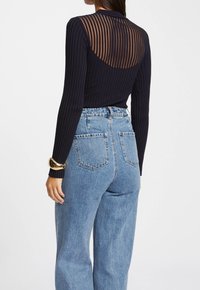 Svart ribbat långärmad topp med en genomskinlig randig rygg, kombinerad med högmidjade ljusblå jeans. Guldarmband på handleden.