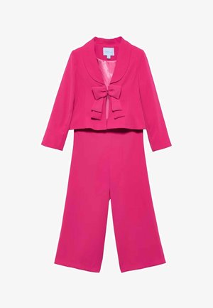 Completo da donna di un rosa acceso, composto da giacca corta con collo sciallato e fiocco decorativo, abbinata a pantaloni a gamba larga.