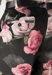 Floral pants featuring a black background with pink and white rose patterns. Includes a back pocket with a dark button and green accent stitching.