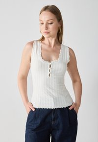 White ribbed tank top with scalloped edges and lace trim, featuring a scoop neckline and three decorative buttons down the front.