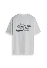 Witte katoenen T-shirt met korte mouwen; heeft een zwart Coca-Cola logo en het woord "Bevete" op de achterkant in een gebogen scriptontwerp.