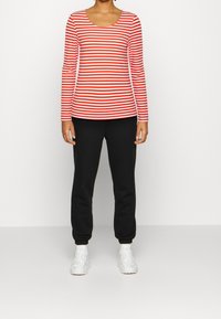 Röd- och vitrandig långärmad topp i kombination med svarta sweatpants och vita sneakers, med en rundad halsringning och figurnära design.