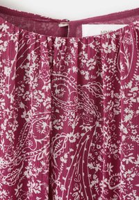 Tissu fluide et à motifs dans un magenta profond avec des dessins floraux blancs et des motifs cachemire ; présente des plis et une fermeture éclair discrète à l'arrière.