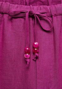 Magenta linnen stof met een elastische tailleband, voorzien van een gestrikt trekkoord en drie decoratieve kralen in verschillende tinten roze.