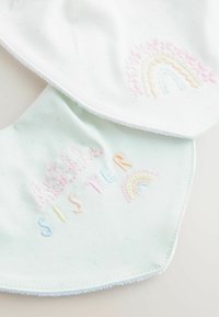 Bavoirs en coton de couleurs pastel, ornés de broderies avec le texte "petite SOEUR" et des motifs arc-en-ciel. Texture douce avec des bords arrondis.
