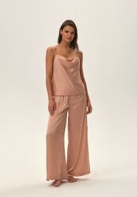Zestaw piżamowy w miękkim różowym satynie, składający się z bezrękawnik z falbaną na dekolcie oraz spodni z szerokimi nogawkami i elastyczną talią.