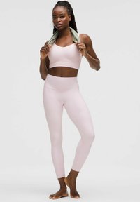 Light pink sports bra with a scooped neckline and matching high-waisted leggings. Smooth texture, fitted design, and a minimalistic style.