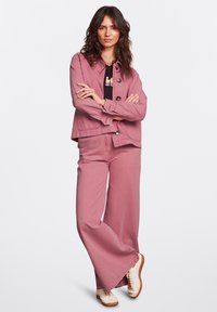 Rosa denimjacka och vida byxor med en svart grafisk t-shirt under. Har stora knappar och krämfärgade sneakers med bruna sulor.