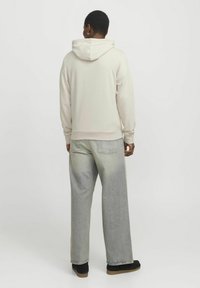 Sudadera beige claro con capucha y cordones, de tejido mezclado, con un corte relajado, combinada con pantalones de mezclilla de pierna ancha en gris claro y calzado negro.
