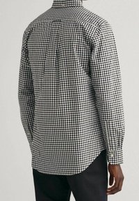 Zwart-wit geruit overhemd met lange mouwen, manchetten met knopen, detail van een rugpas en een afgeronde zoom. De stof oogt glad met een gestructureerde pasvorm.