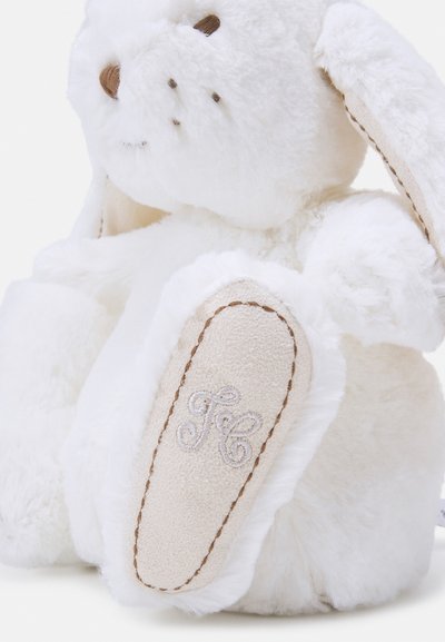 Jouet en peluche blanc en forme de lapin avec de longues oreilles, un nez brodé marron et des accents cousus. Le pied est en tissu beige avec les initiales monogrammées "JC."