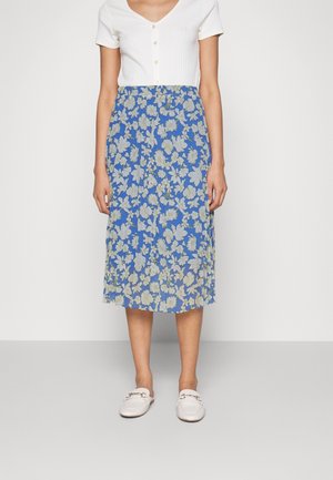 Niebieska midi spódnica w kwiaty z jasnym żółtym i białym wzorem, zestawiona z białym prążkowanym topem i białymi wsuwanymi butami. Gładka tekstura tkaniny.