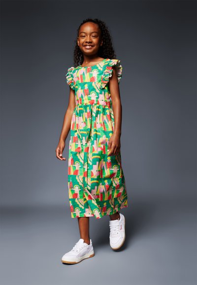 Πράσινο βαμβακερό φόρεμα με ριχτές ώμους, παρουσιάζοντας ένα πολύχρωμο μοτίβο από αφηρημένες μορφές. Ριγέ σχέδιο και μήκος μέχρι τον αστράγαλο. Λευκά αθλητικά παπούτσια.