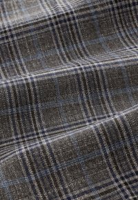 Gros plan d'un tissu texturé avec un motif à carreaux gris, bleu et noir et des détails de tissage visibles.
