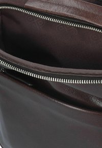 Interno di una borsa in pelle marrone con una fodera scura, cerniera argentata e tasche organizzate per riporre gli oggetti. Texture liscia con dettagli di cucitura sottili.
