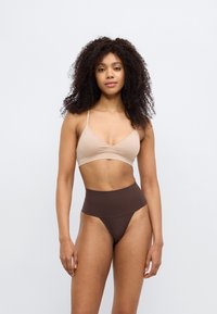 Μπεζ σουτιέν με λεπτές τιράντες συνδυασμένο με καφέ μαγιό σλιπ ψηλόμεσο. Λείο υλικό, μίνιμαλ σχέδιο, χωρίς ορατά μεταλλικά στοιχεία.