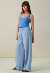 Débardeur bleu clair associé à un pantalon large texturé bleu. La tenue présente une taille élastique et est complétée par des sandales noires.