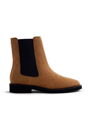 Bottine en daim beige avec un bout arrondi, des panneaux latéraux élastiques et une semelle en caoutchouc noir. Le design présente des lignes épurées et un détail minimal.