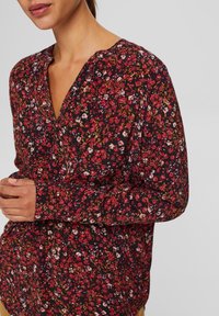 Sort blomsterbluse med V-hals, lange ærmer og en samlet detalje. Små røde, lyserøde og gule blomster på en mørk baggrund.
