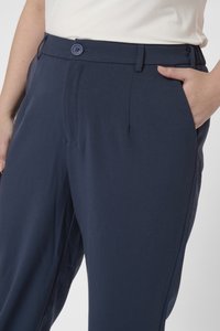 Pantalones azul marino con una textura suave, que cuentan con un botón frontal y bolsillos laterales. La cinturilla es plana, con un corte ajustado y pinzas.