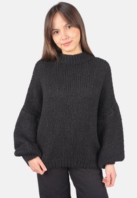 Schwarzer Strickpullover mit hohem Ausschnitt, strukturiertem Stoff und übergroßen Ärmeln, kombiniert mit dunkler Hose.