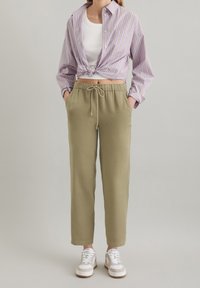 Ljuslila randig skjorta med knut i midjan, vit t-shirt, olivgröna byxor med elastisk midja och vita sneakers med grå detaljer.