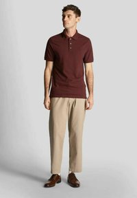 Polo color mogano con maniche corte e abbottonatura a tre bottoni, abbinata a pantaloni beige larghi e scarpe eleganti marroni. Design semplice e classico.