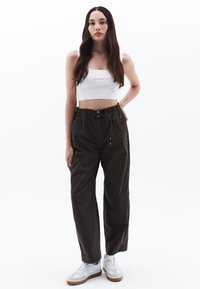 Zwarte, loszittende broek met een elastische tailleband en trekkoord, gecombineerd met een witte cropped tanktop en witte sneakers.