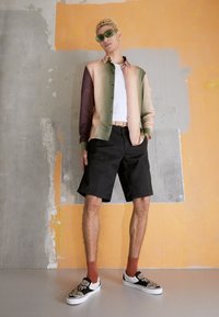 Camisa de botones con degradado de color de rosa a verde, pantalones cortos negros, zapatillas de slip con estampado, y gafas de sol retro verdes.