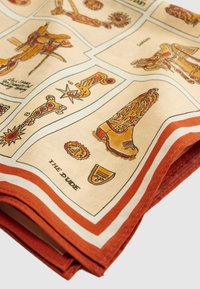 Διπλωμένο ύφασμα με πολύχρωμες, vintage εικόνες από δυτικά μποτάκια, αγκράφες και αξεσουάρ, με κόκκινη και λευκή ριγέ κορνίζα.