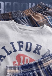 T-shirt en coton gris avec imprimé graphique, col à revers ; deux paires de shorts à carreaux multicolores avec tailles élastiquées dans des tons bleus et beiges.