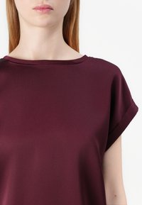 Bordeaux kortermet bluse med bred halslinje. Laget av glatt stoff, med oppbrettede ermer og en avslappet passform.