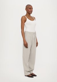 Lichtgrijze, high-waisted, geplooide broeken gecombineerd met een aansluitend wit tanktop. Model draagt donkere, platte schoenen. Gladde, lichtgewicht stof.