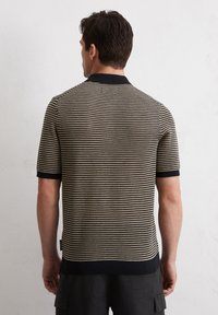 Gebreide poloshirt met korte mouwen, voorzien van een zwart en crèmekleurig zigzagpatroon, geribde kraag en manchetten, en een rechte zoom.