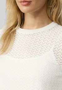 Witte gebreide top met een zigzagpatroon en een effen onderpaneel. De halslijn is rond met een geribbeld textuur.